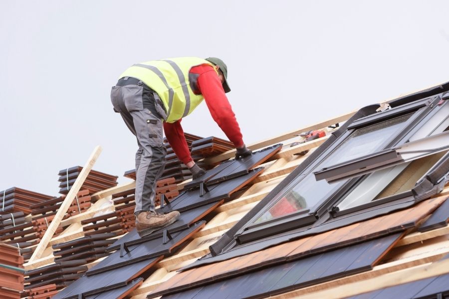 Construction worker placing roof tile on roof